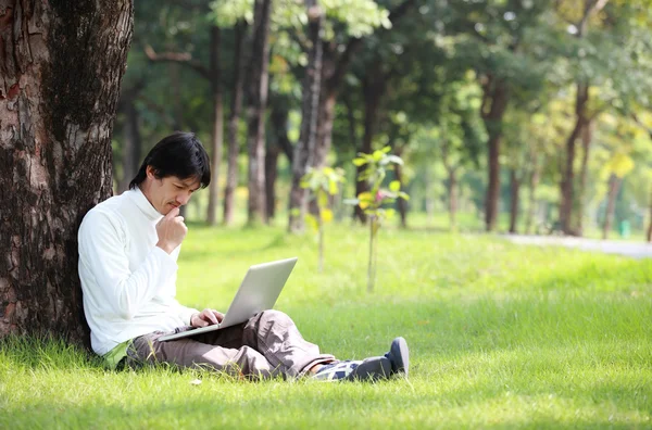 Молодой человек использует свой ноутбук на траве — стоковое фото