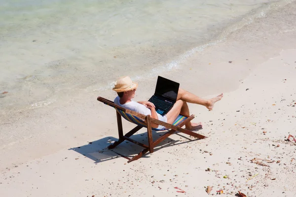 Człowiek siedzi na leżaku z laptopa na plaży — Zdjęcie stockowe