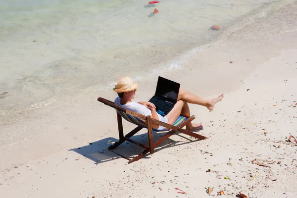 Άνδρα που, καθισμένος σε μια ξαπλώστρα με ένα φορητό υπολογιστή στην παραλία — Φωτογραφία Αρχείου