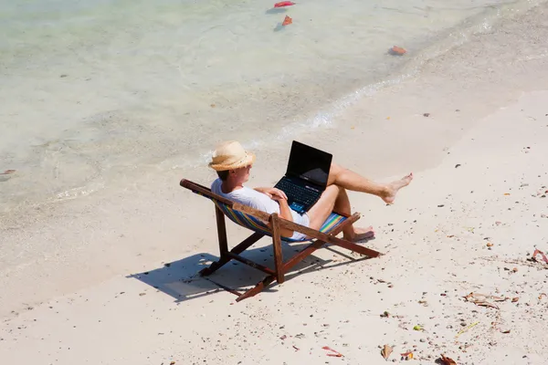 Człowiek siedzi na leżaku z laptopa na plaży — Zdjęcie stockowe