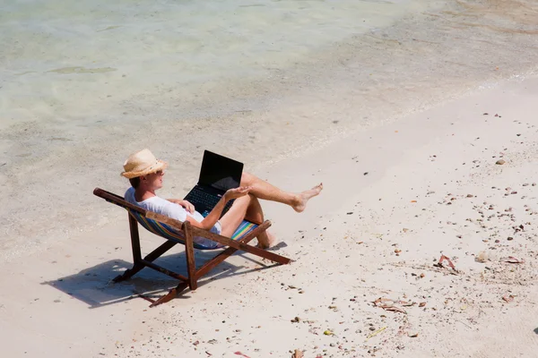 Człowiek siedzi na leżaku z laptopa na plaży — Zdjęcie stockowe