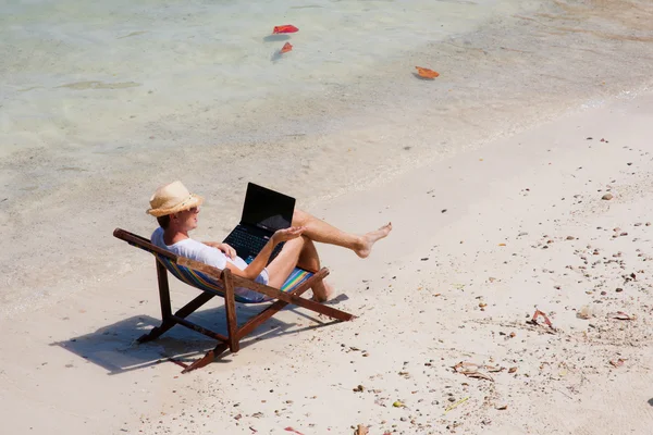Man zit op een ligstoel met een laptop op het strand — Stockfoto