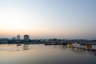 Güneşin doğuşunun ya da batışının şehir görüntüleri. Bangkok Tayland 'da römorkör ile nehir üzerinde köprü.