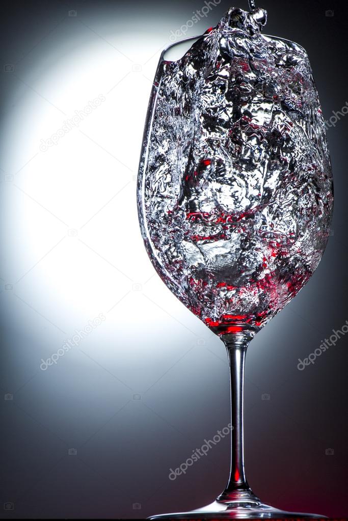 Wine glass filled with moving liquid splashes of red.