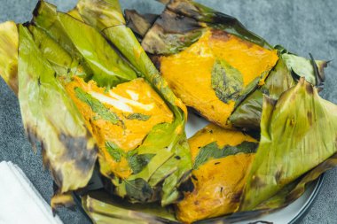 Muz yaprağında köri ezmesiyle buharda pişirilmiş deniz ürünleri.