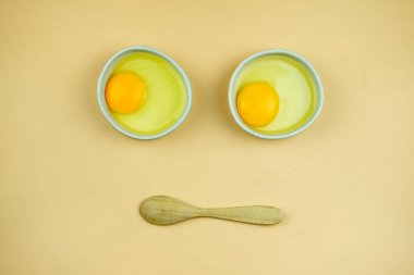 Küçük beyaz kâse ve tahta kaşıkta çiğ yumurta. Yüzün komik şekli, Üst Görünüm