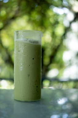 Soğuk yeşil çay milkshake 'i bardakta, arka planda.