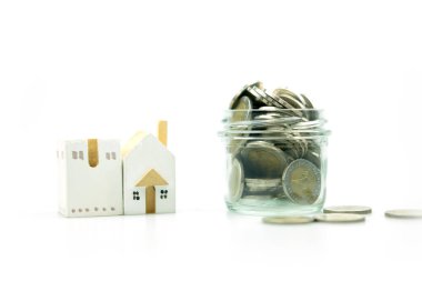 Kavanozun yanında beyaz arka planda tam paralar olan bir ev modeli. Metin için boşluk