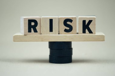 Tahta tahtadan tahtadan tahterevallinin üzerinde dengelenen RİSK sözcüğü alfabeyle birlikte küp tahta blok. Risk değerlendirmesi, iş görüşmelerini kabul etme kararı belirsizliğe, öngörülemez durum konseptine yol açar