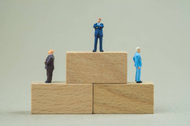 Minyatür insanlar: Tuğlanın üzerinde duran iş adamı ve karar vermek için sağda solda duran iki işadamı. İş konsepti, anlaşma, başarı ve başarı.