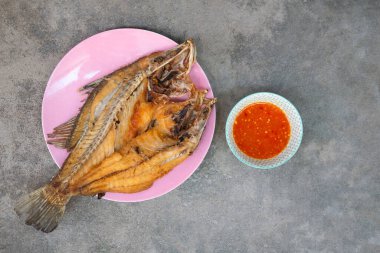 Balık soslu kızarmış levrek, arka planda acı biber sosuyla servis ediliyor..