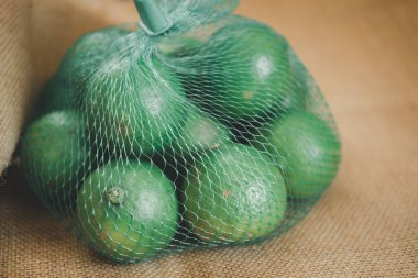 Ağ yeşil plastik bir ağ içinde paketlenmiş taze yeşil limonlar.