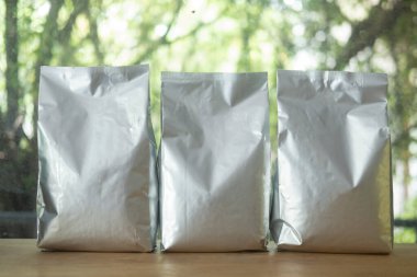 Üç adet folyo plastik poşet. Tahta masaya konmuş.