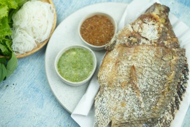 Baharatlı sos, tatlı sos ve sebzeyle servis edilen tuzlu kabuklu ızgara balık. Kapat.