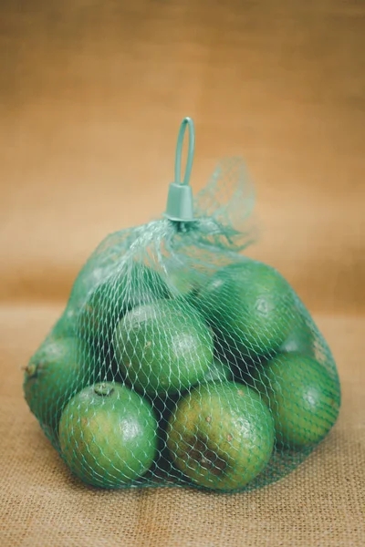 緑のプラスチック製のメッシュ袋に新鮮な緑のレモンのクローズアップ — ストック写真