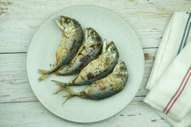 Tahta masadaki beyaz seramik tabakta servis edilen kızarmış uskumrunun hemen üstünde. Taylandlı Pla Too Tod, ünlü Tayland yemeği.