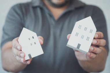 Bir erkek, iki ahşap evi kiralamak ya da satın almak için tutuyor. Gayrimenkul kavramı ve konut veya ev değerlendirmesi konsepti