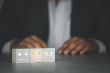 Müşteri hizmetleri değerlendirmesi ve memnuniyet araştırması konseptleri. Tahta küpteki yüz simgesi ve yüz ifadeleri tatmin edici bir gülümseme..