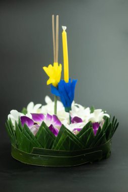 Tayland dolunayı için çiçeklerle süslenmiş üç tütsü çubuğu ve mumları olan muz yaprağı Krathong ya da siyah arka planda izole edilmiş Loy Krathong festivali.