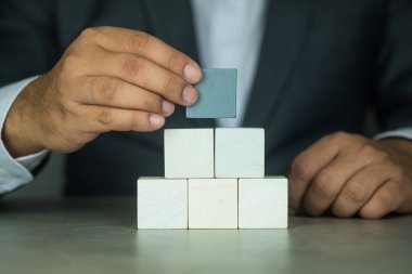 Businessman hand putting and stacking blank wooden cubes on table with copy space for input wording and infographic icon.