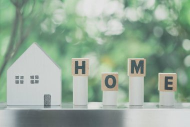 Text HOME on wood blocks and wood home on nature background. Conceptual image of first home and saving for buy home.