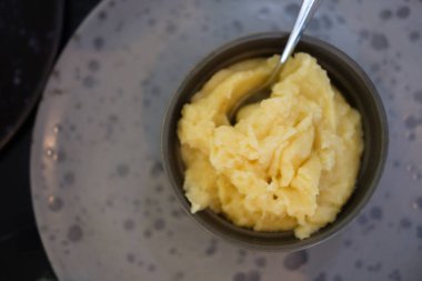 Mashed potatoes in a black bowl with spoon. Top view