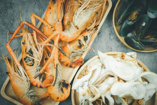 Cooked seafood shrimps, squid and mussels served on wooden plate. The concept of seafood delivery