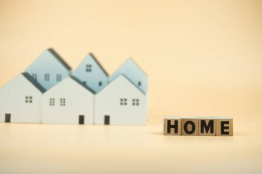 A wooden cube with the letter the word HOME with the miniature white home background. The conceptual image of first home and saving for buy home.