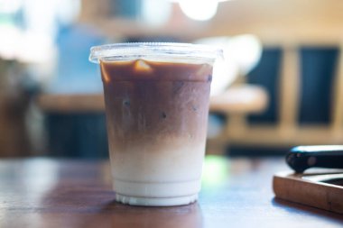 Plastik bardakta 16 ons buzlu latte kahve. Kafedeki ahşap masada.