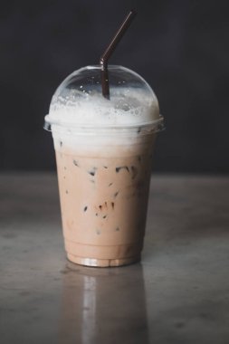Kahve dükkanının masasında plastik bardakta buzlu kahve ve süt köpüğü.