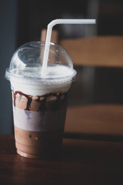 Tahta bir masada sütlü plastik bir bardak buzlu kahve..