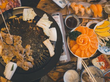 Kızarmış tavada ızgara domuz eti, diğer mezeler ve açık büfede somon suşisi. Japon ve Kore yemekleri konsepti.