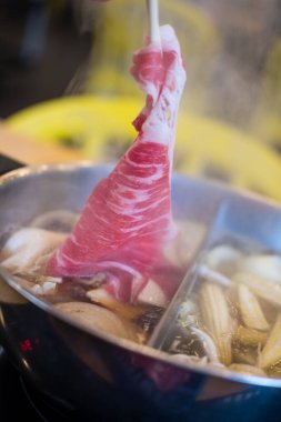 Chopstic holding beef shabu-shabu veya sukiyaki. Biftek dilimi sıcak tencerenin üstünde. Japon shabu-shabu veya Sukiyaki.
