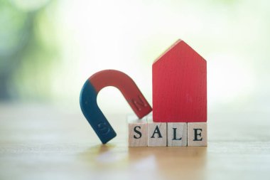 Red home and magnet put on the top wooden block cube with text SALE on sunlight in the nature.