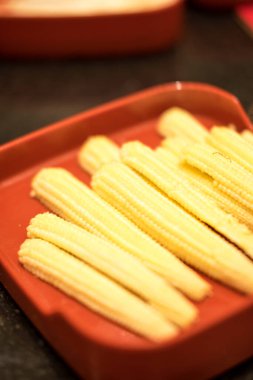 Sıcak tencerede pişirmek için kırmızı tepside çiğ mısır.