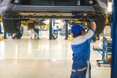 Üniformalı yakışıklı tamirciler kaldırılmış araçla otomobil servisinde çalışıyorlar. Araba tamiri ve bakımı.