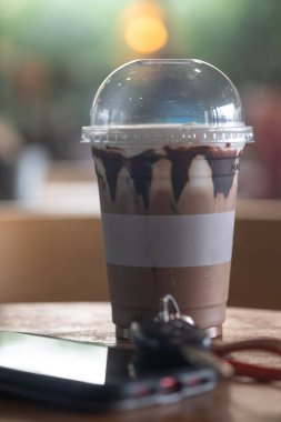 Kahve dükkanındaki ahşap masanın üzerinde plastik bardakta buzlu kahve.