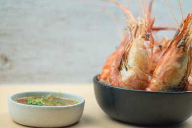 Kaynamış bir nehir karidesi. Büyük bir kısmı deniz ürünleri sosuyla servis edilen siyah kasede.