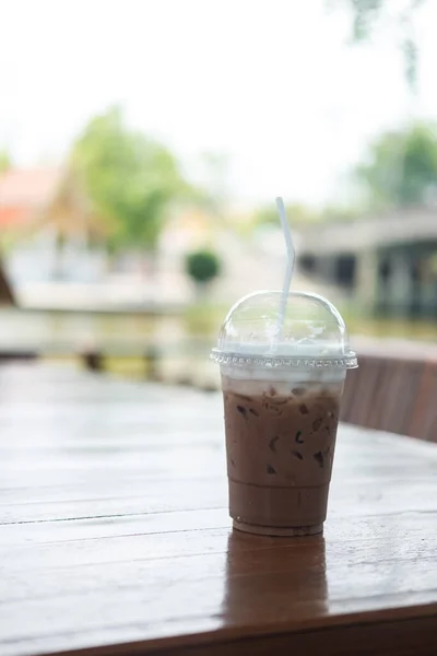 Iced coffee in take away cup on the outdoor wood table at cafe.