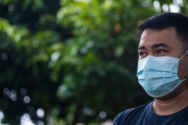Asian man wearing a protection mask against PM 2.5 air pollution and flu with nature blur light. Stay at home to prevent the spread of the virus.