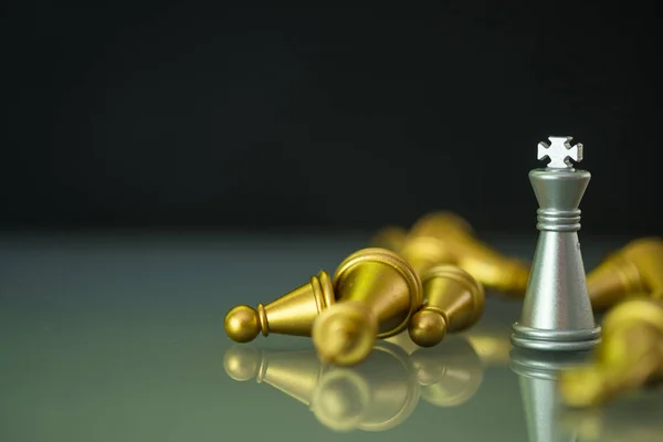 A silver king who stands in falling golden chess on chessboard. Chess game and competition concept.