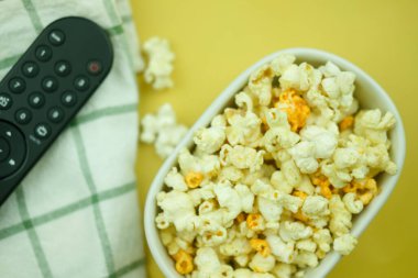 Beyaz seramik patlamış mısır kasesini ve uzaktan kumandayı kapat. Ev sineması ve ev konseptinde film ya da dizi izlemek.