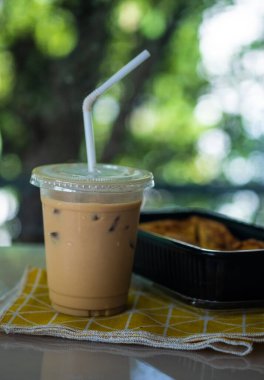 Iced coffee latte and breakfast in black box against nature background.