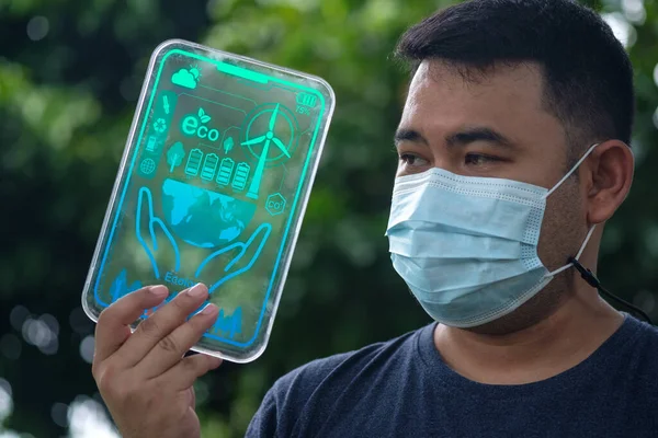 Young man holding a futuristic transparent glass tablet with the dashboard of renewable energy resources. The technological solutions, green energy concept energy sources sustainable. Ecology elements