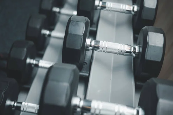 Rows of metal dumbbells on rack for strength training in gym. Close up