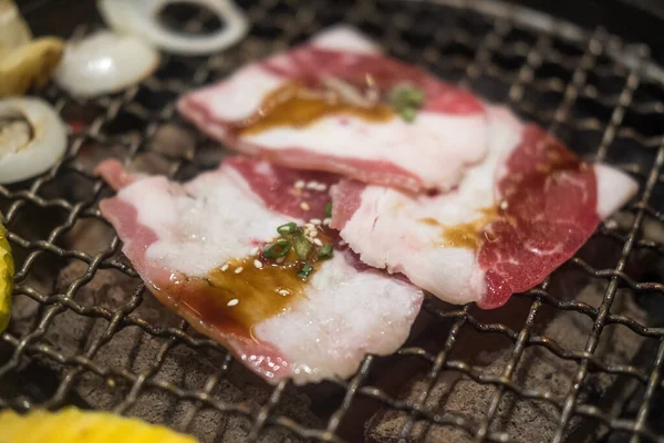 Grilling raw beef on metal grill pan over hot charcoal stove, Japanese barbecue style, Yakiniku.