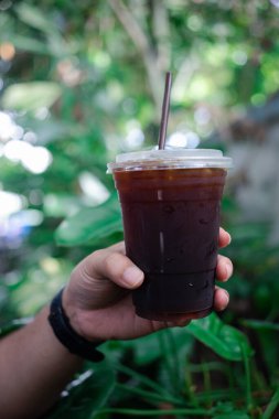 Sabahları elinde bir bardak buzlu kahve ile bahçenin arka planında....