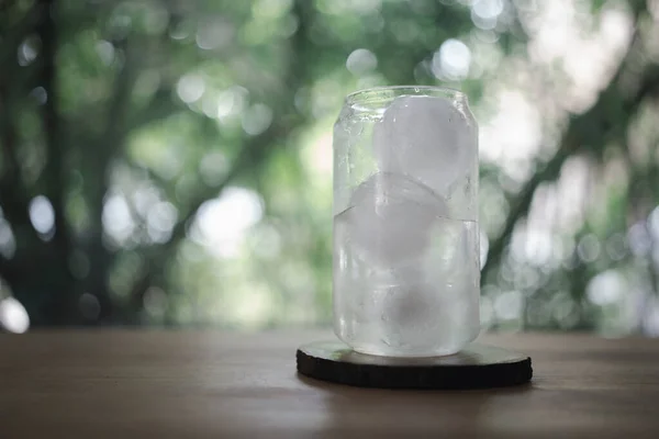 A glass of water with ice ball on wood table