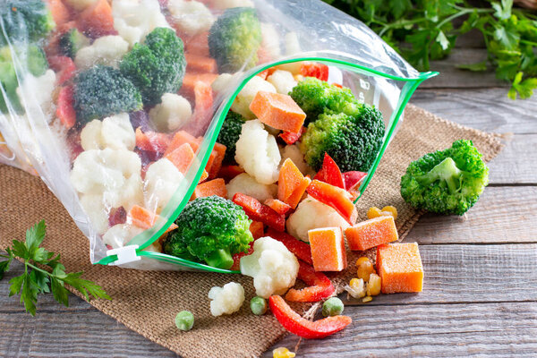 Plastic bags with different frozen vegetables on a wooden table. Food storage