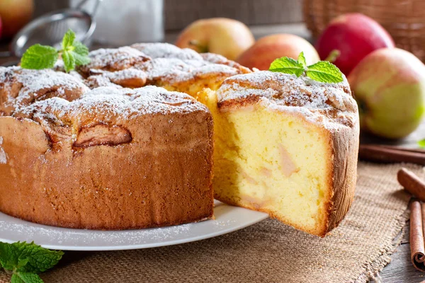 Homemade round sponge cake or chiffon cake with apples on white plate so soft and delicious with ingredients: eggs, flour, milk on wooden table. Homemade bakery concept for background and wallpaper.